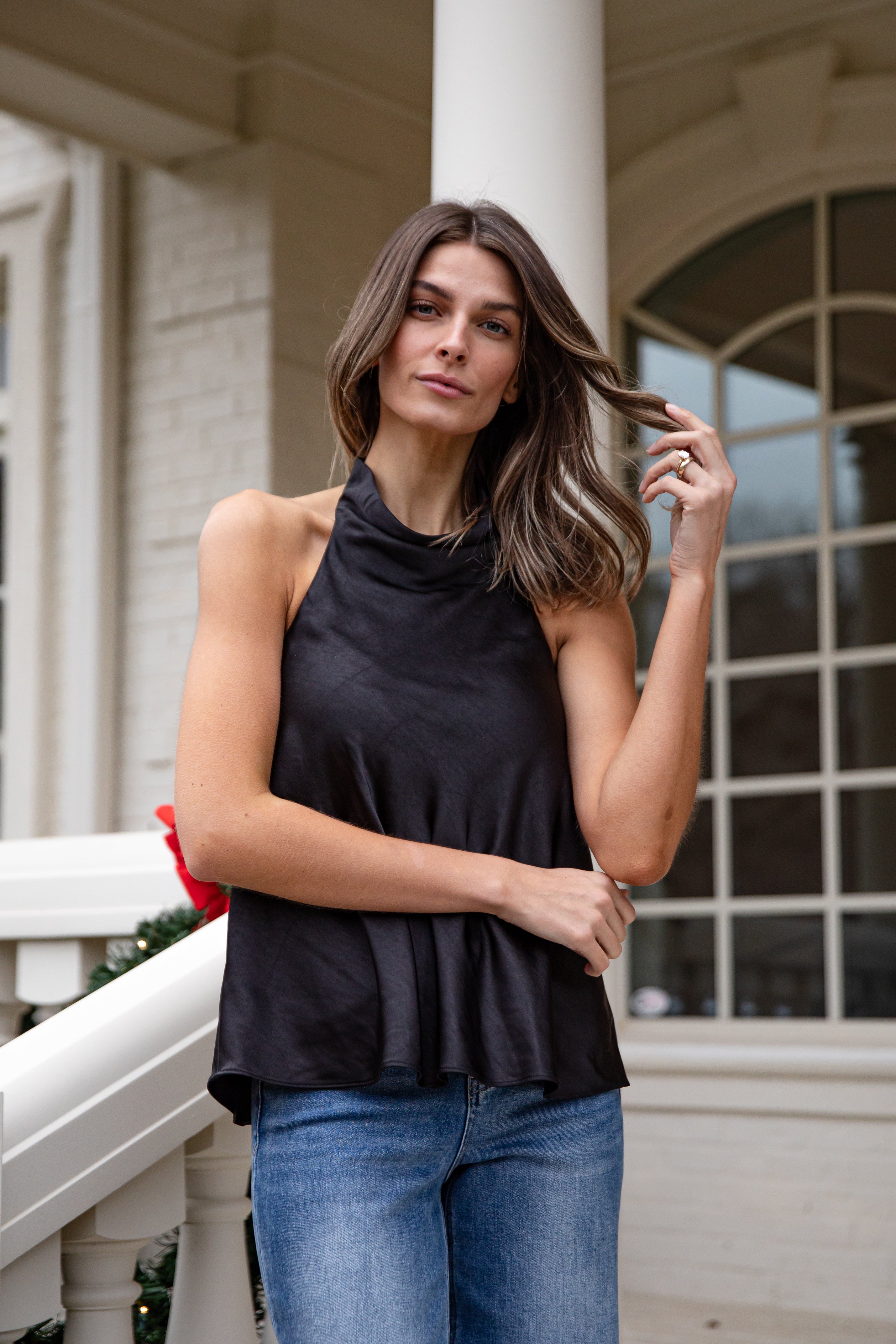 Woman wearing a black sleeveless top and blue jeans standing on a porch.