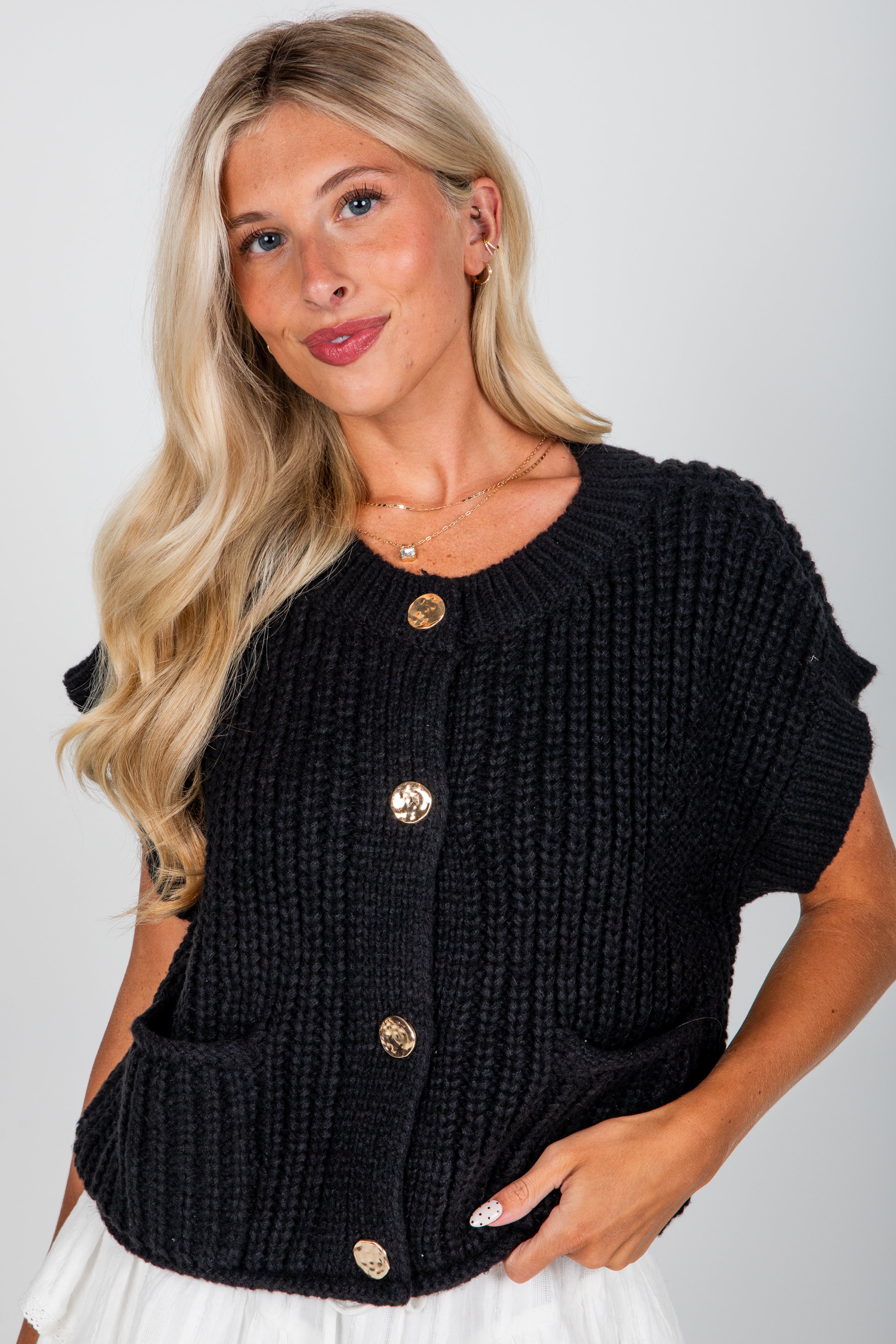Woman wearing a black knitted cardigan with gold buttons on a white background