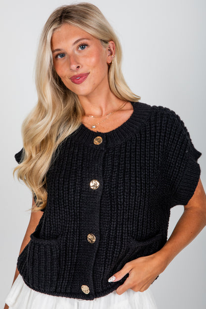 Woman wearing a black knitted cardigan with gold buttons on a white background