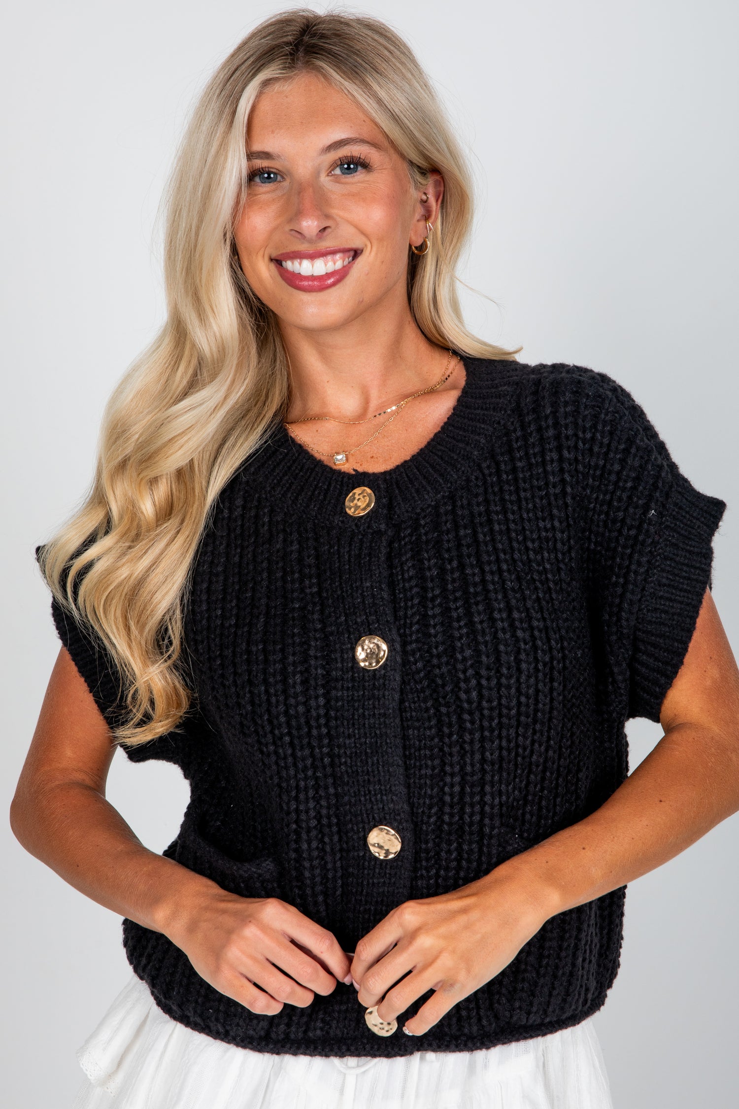 Woman wearing a black knitted cardigan with gold buttons on a white background