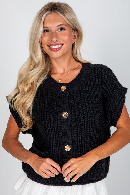 Woman wearing a black knitted cardigan with gold buttons on a white background