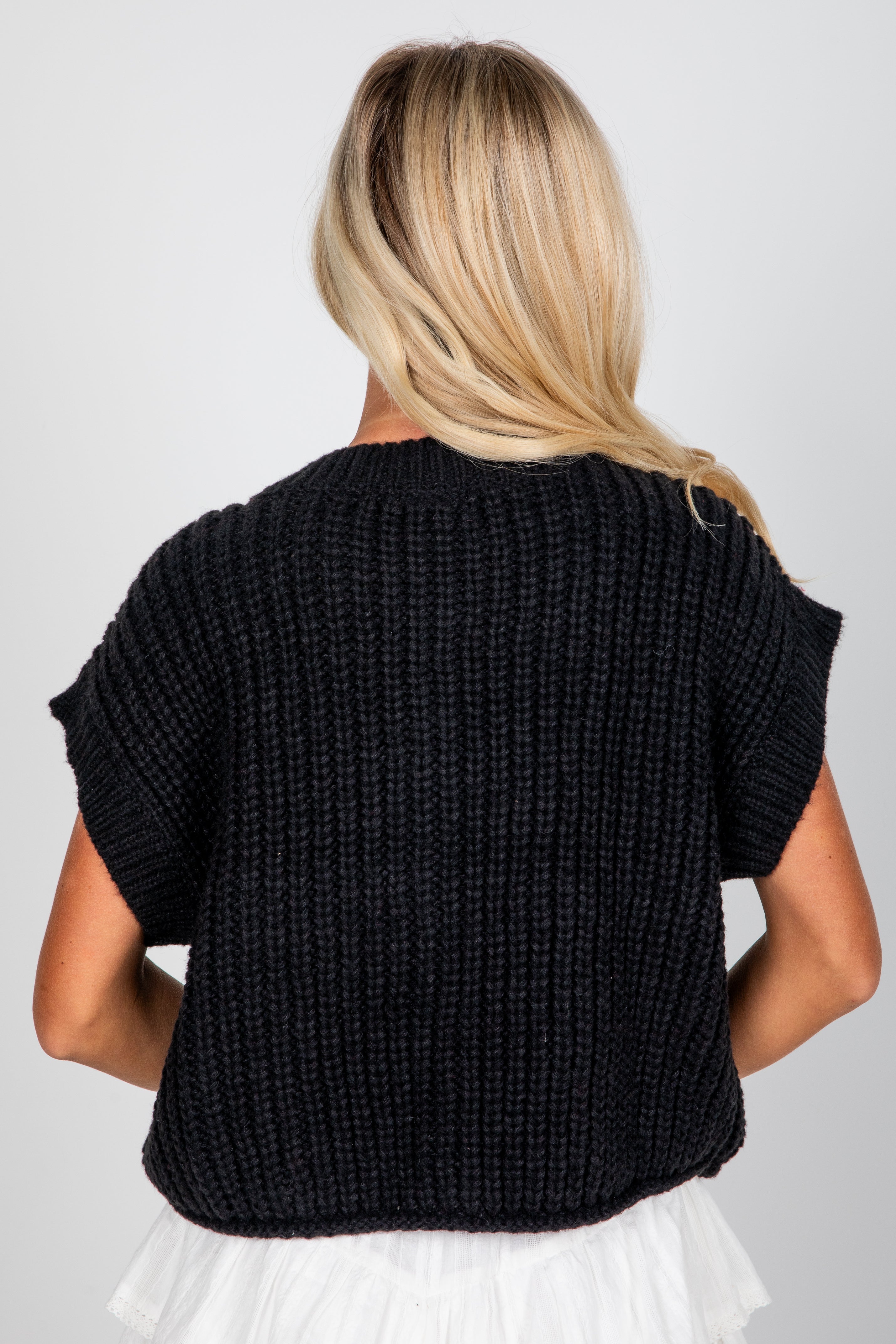 Woman wearing a black knitted sleeveless sweater on a white background