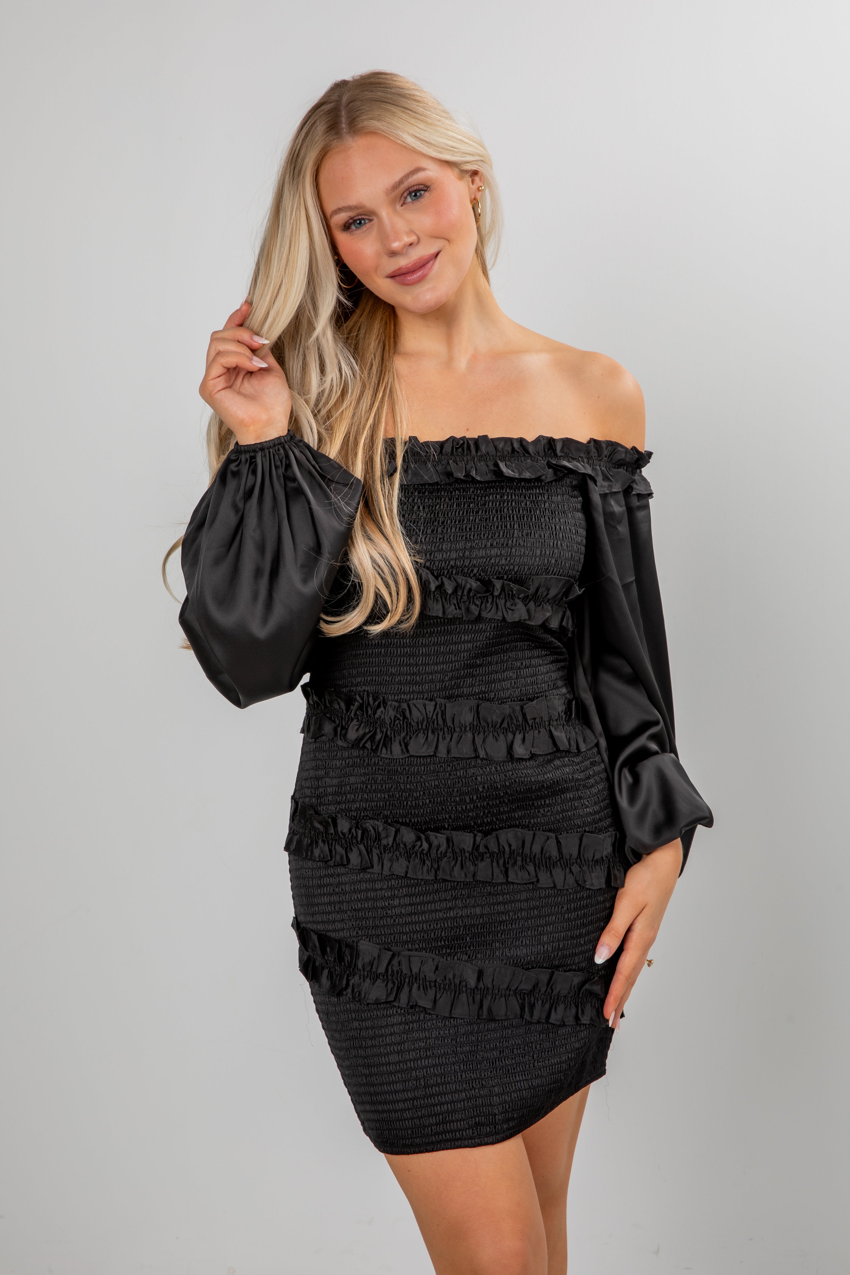 Woman wearing a black off-shoulder dress with ruffled details on a plain background
