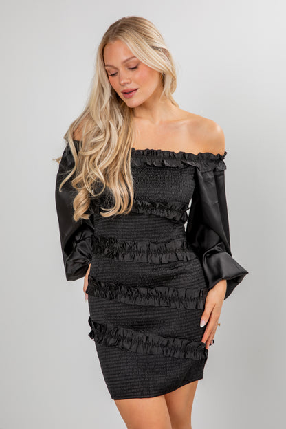 Woman wearing a black off-shoulder dress with ruffled details on a gray background