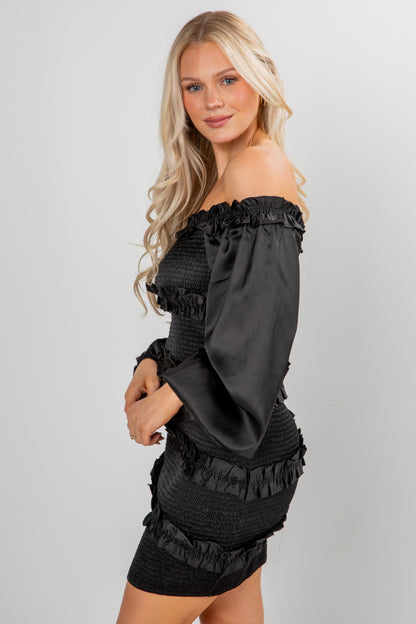 Woman wearing a black off-shoulder dress with ruffled details on a gray background