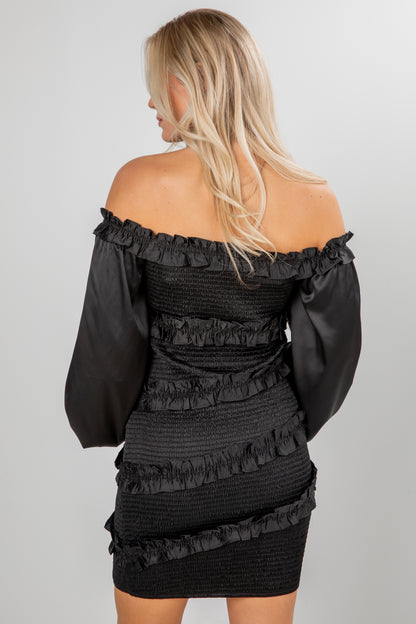 Black off-shoulder dress with ruffled details on a plain background