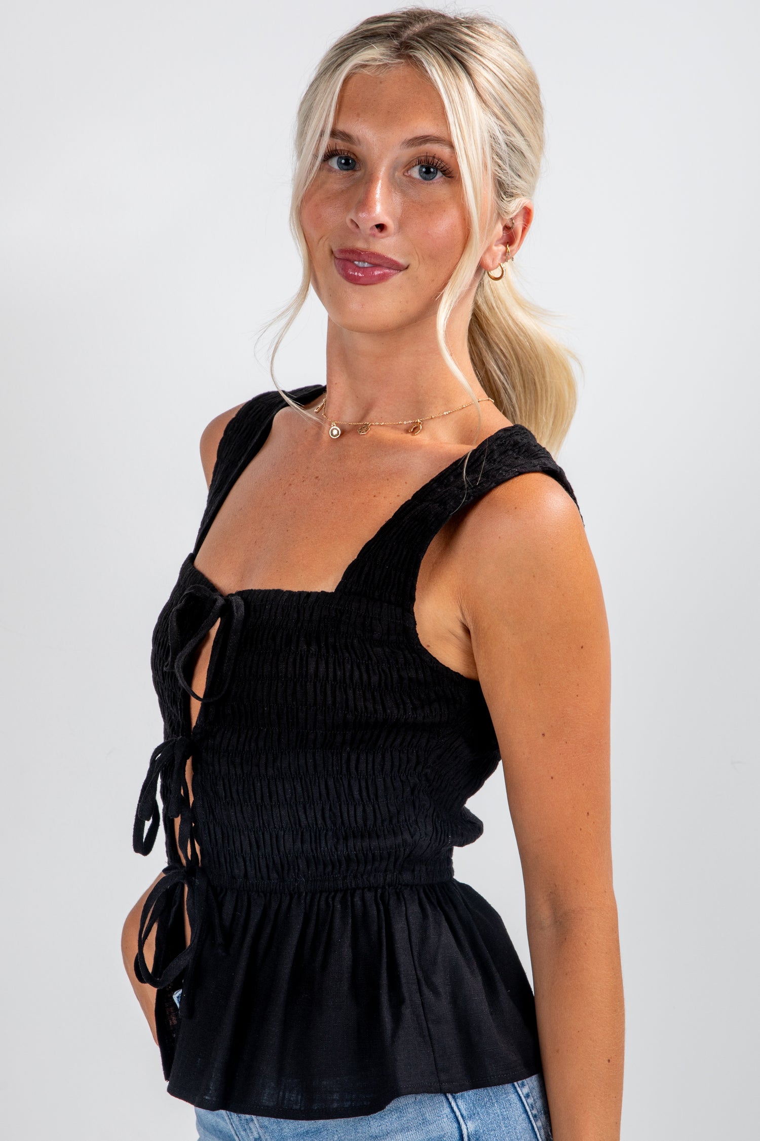 Woman wearing a black sleeveless top with lace-up details on a plain background
