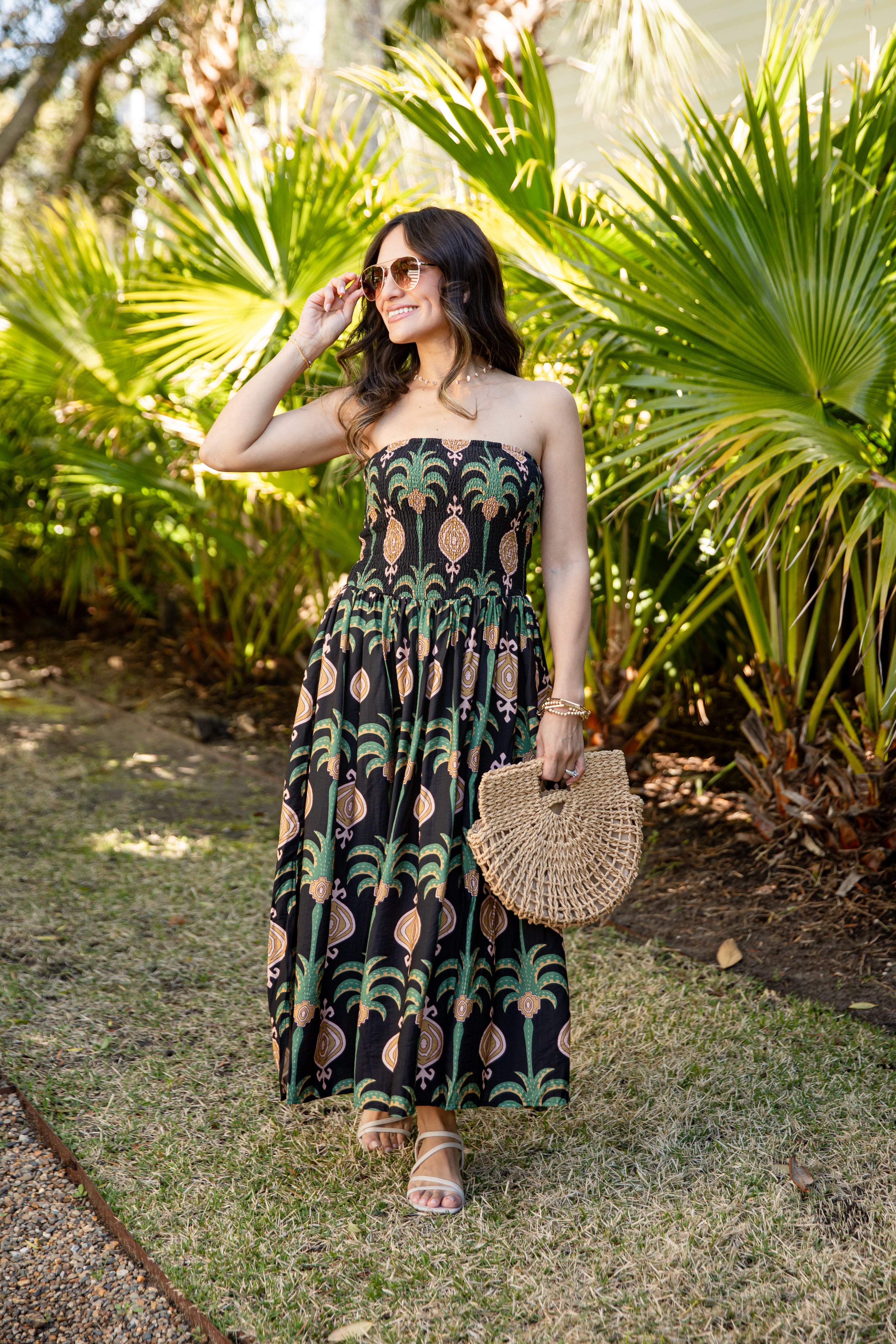 Woman in a strapless dress with palm tree pattern standing in a garden.