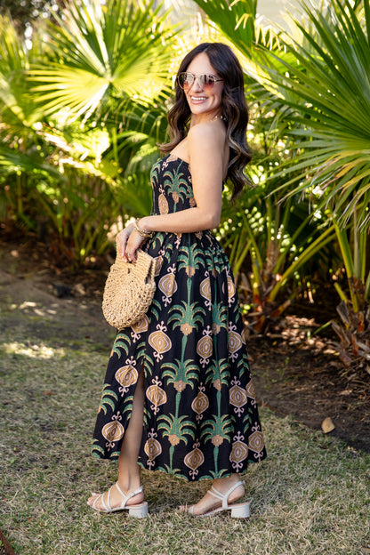 Woman in a patterned dress standing in a tropical setting with palm trees.