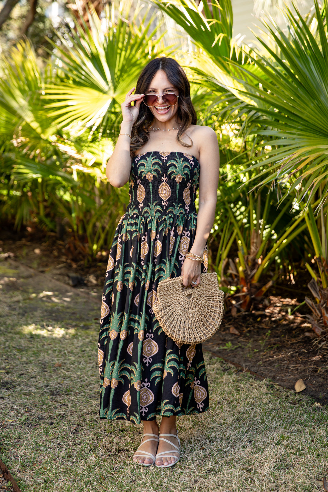 Woman in a strapless dress with a leaf pattern standing in front of palm trees.