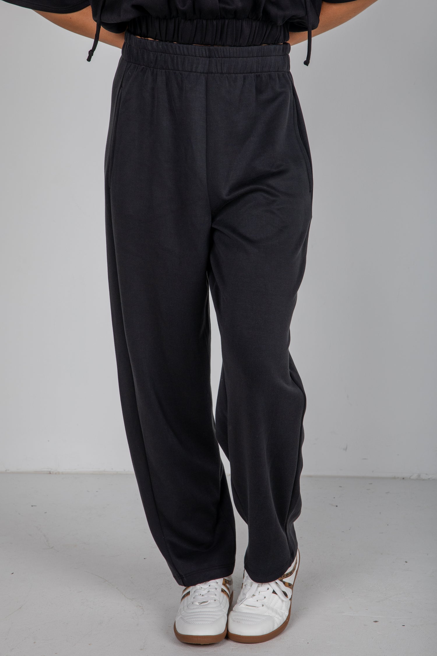 Person wearing black pants and white sneakers on a plain background