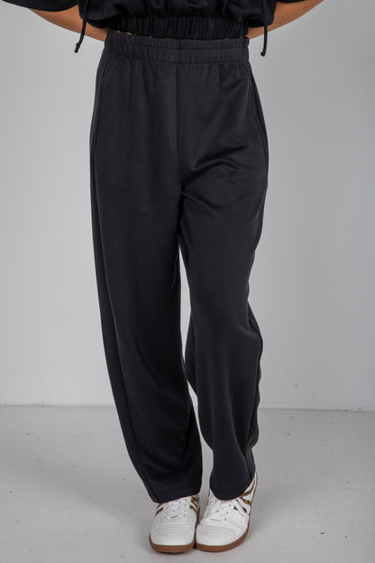 Person wearing black pants and white sneakers on a plain background