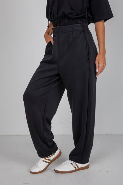 Person wearing black wide-leg pants and white sneakers on a plain background