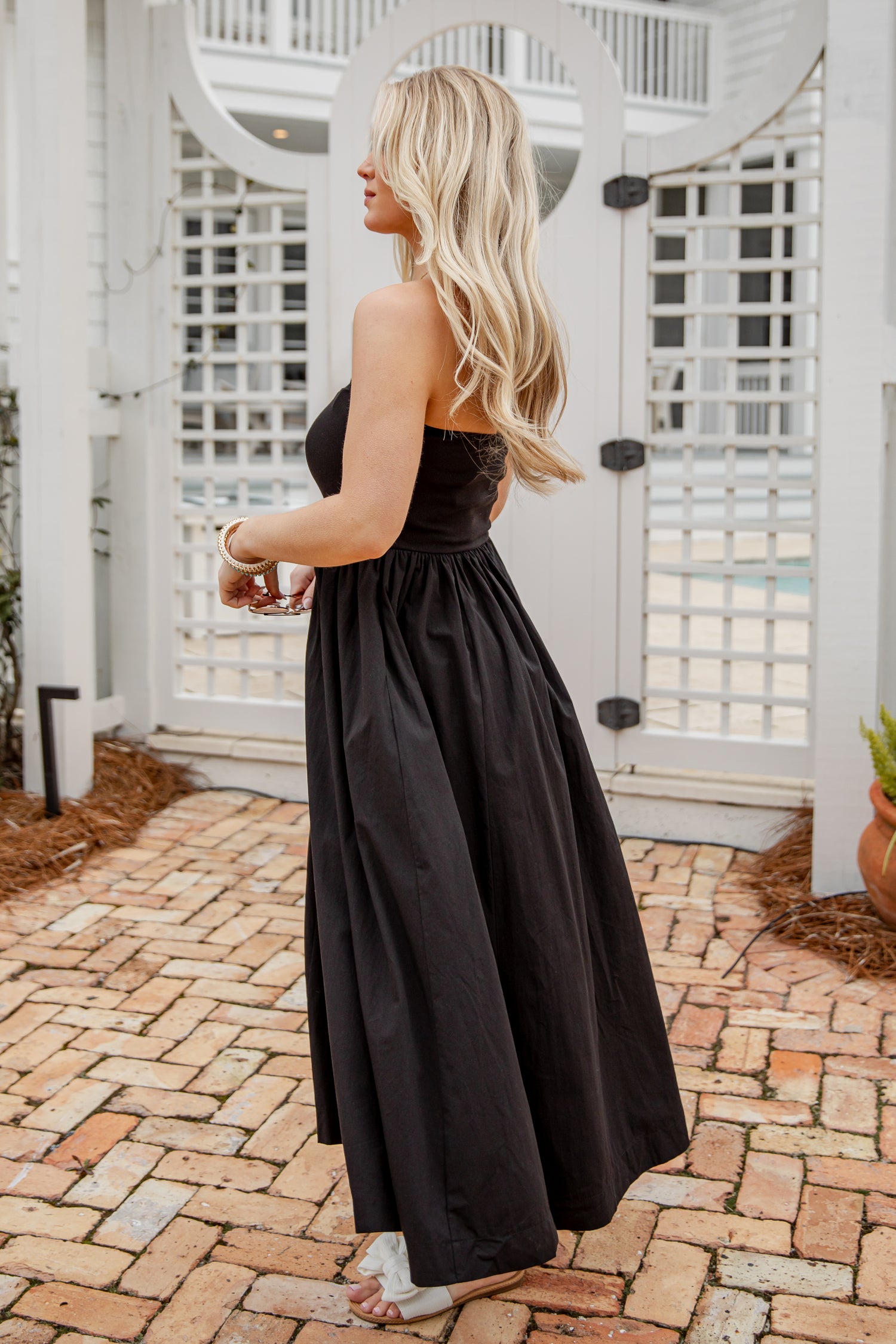 Woman in a black strapless dress standing on a brick patio.