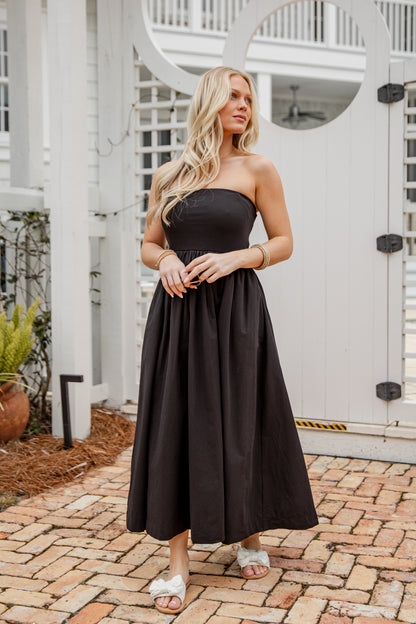 Woman in a black strapless dress standing on a brick patio.