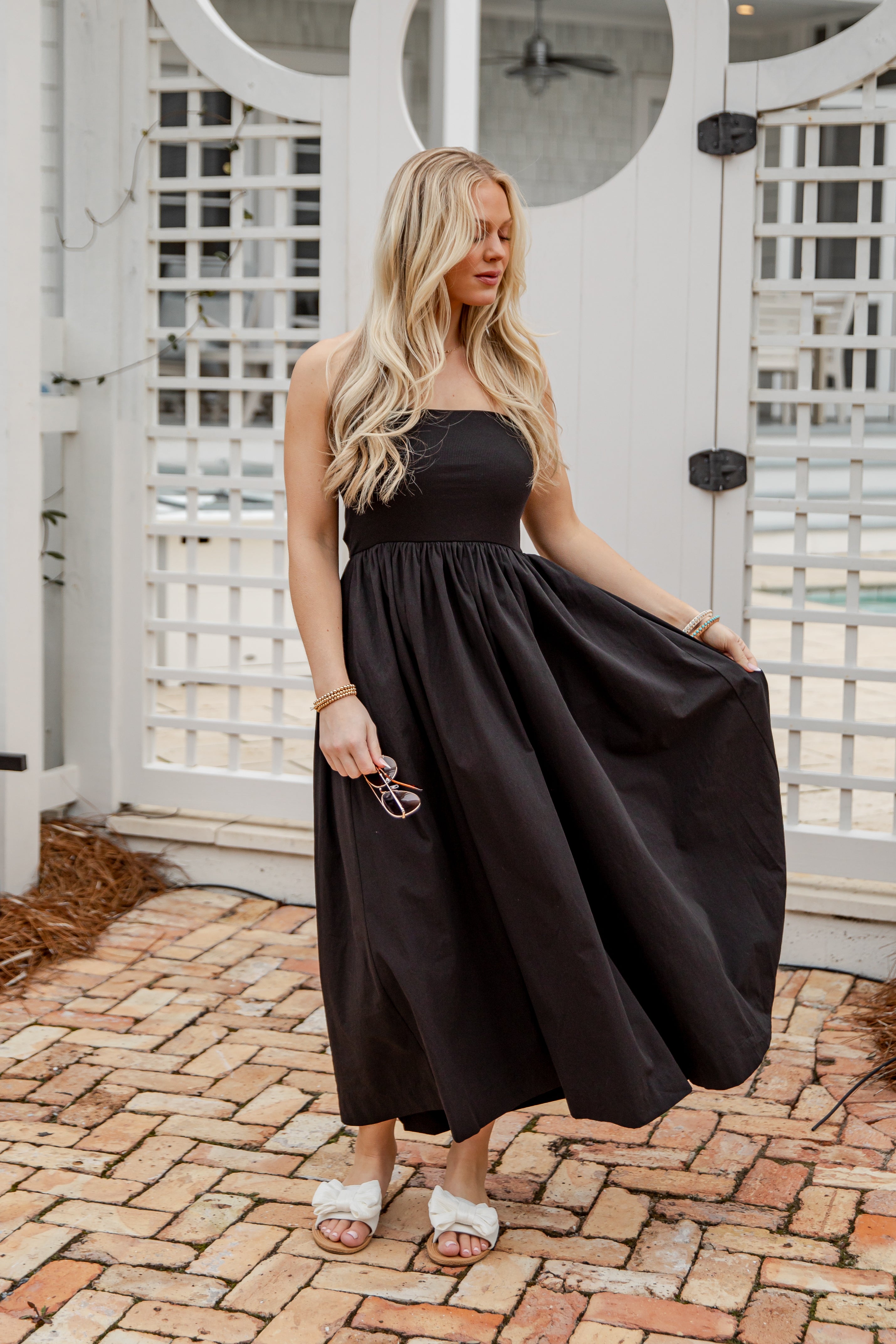 Woman in a black dress standing on a brick patio with a white lattice background
