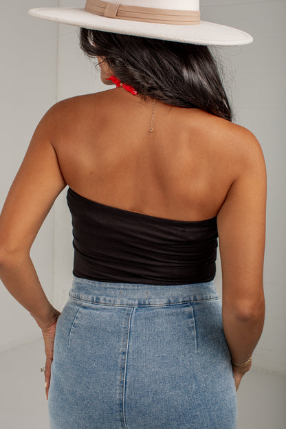 Rear view of a woman wearing a black strapless bandeau top, a light blue denim skirt, and a white wide-brim hat.