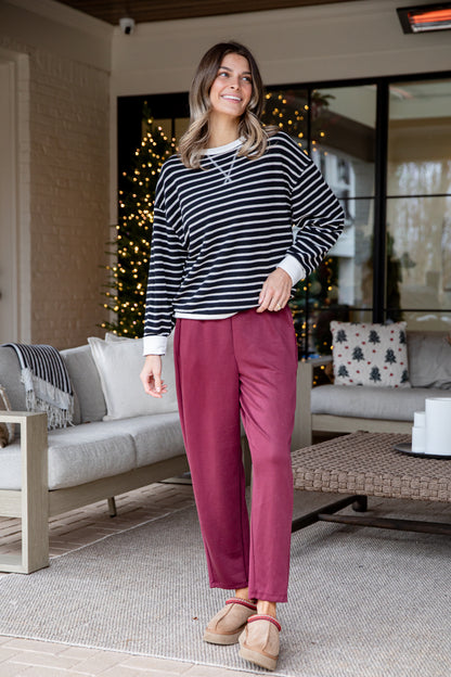 Woman standing in a living room wearing a striped sweater and pink pants.