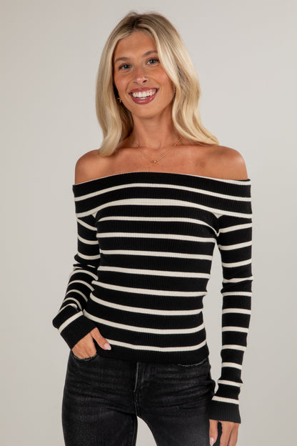 Woman wearing a black and white striped off-shoulder top against a plain background