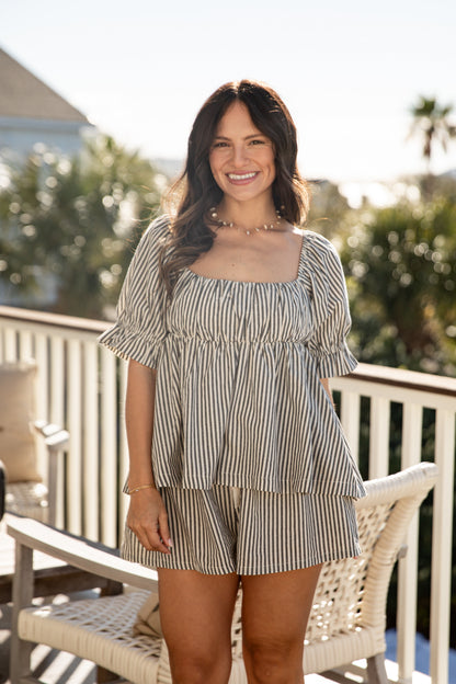 Woman in a striped dress sitting on a chair outdoors with trees in the background