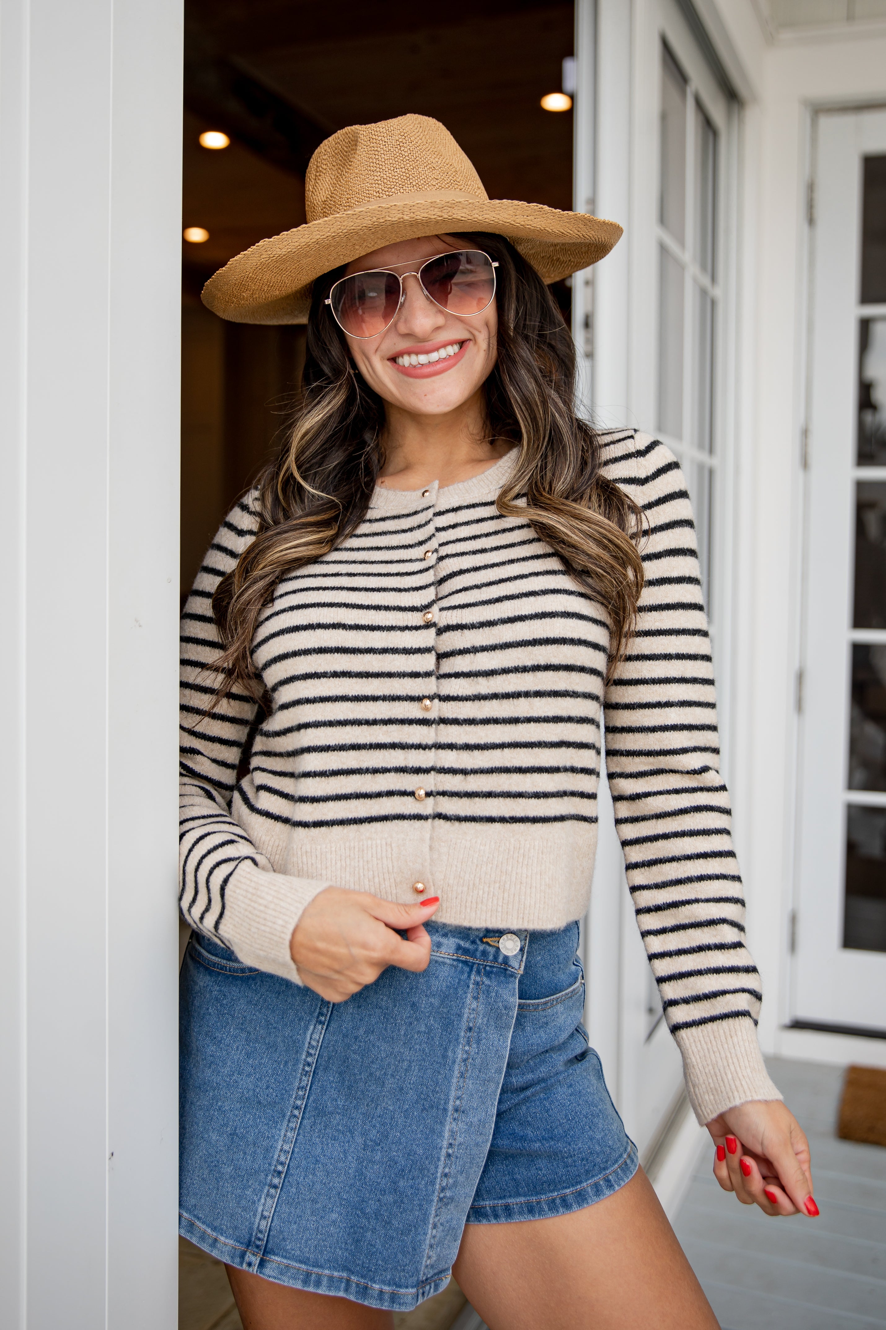Woman wearing a striped sweater, denim shorts, and a wide-brimmed hat outdoors.