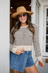 Woman wearing a striped sweater, denim shorts, and a wide-brimmed hat outdoors.