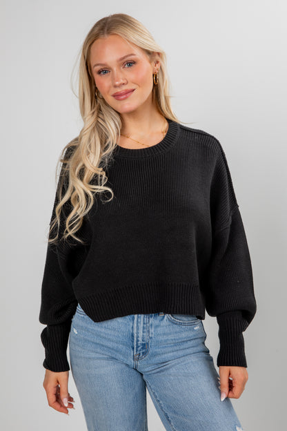 Woman wearing a black sweater and blue jeans against a gray background