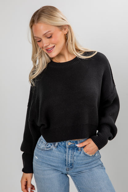 Woman wearing a black sweater and blue jeans on a gray background