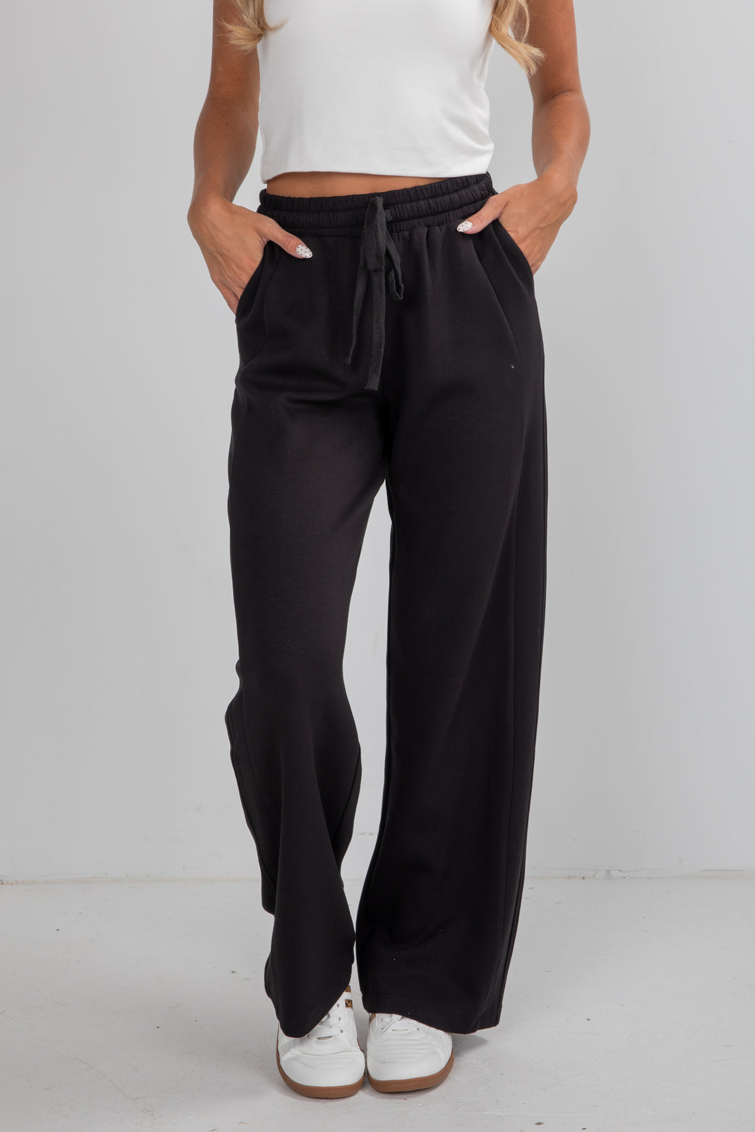 Person wearing black wide-leg pants with a white top on a plain background