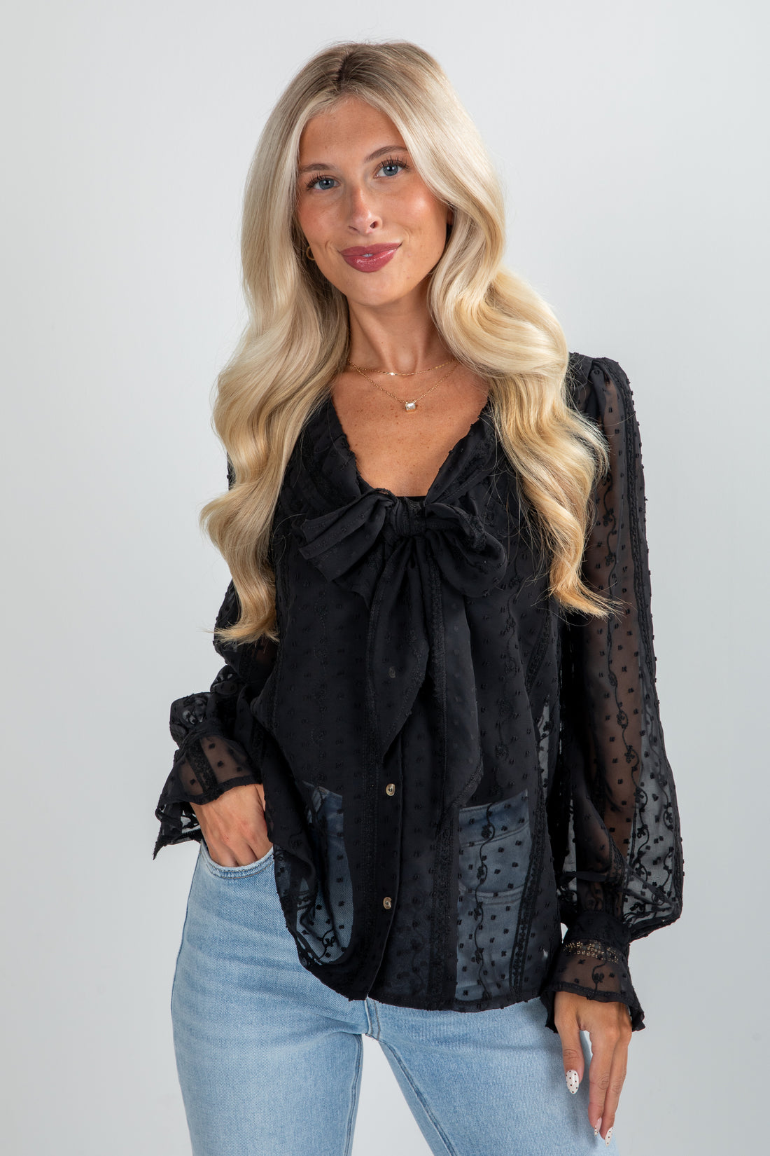 Woman wearing a black blouse with sheer sleeves and light blue jeans on a plain background