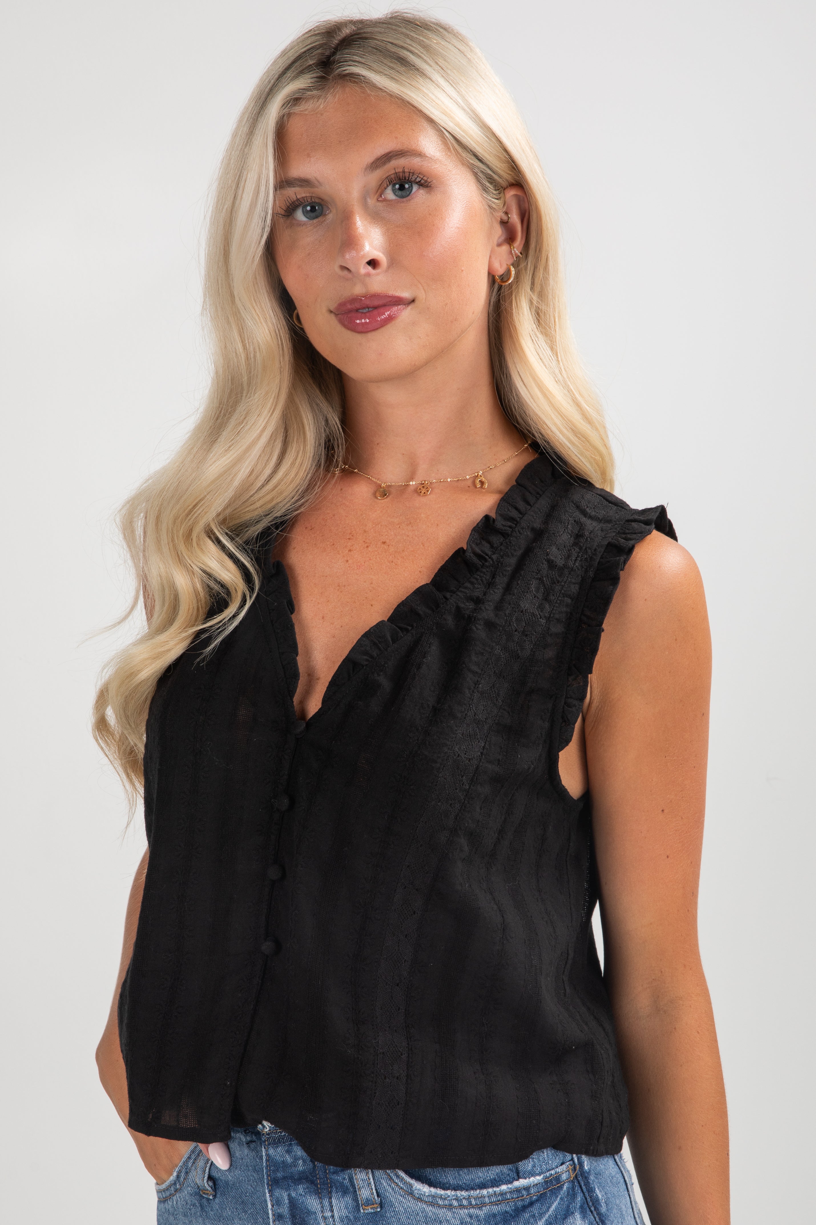 Woman wearing a black sleeveless top with ruffled details against a plain background