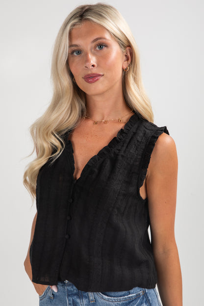 Woman wearing a black sleeveless top with ruffled details against a plain background