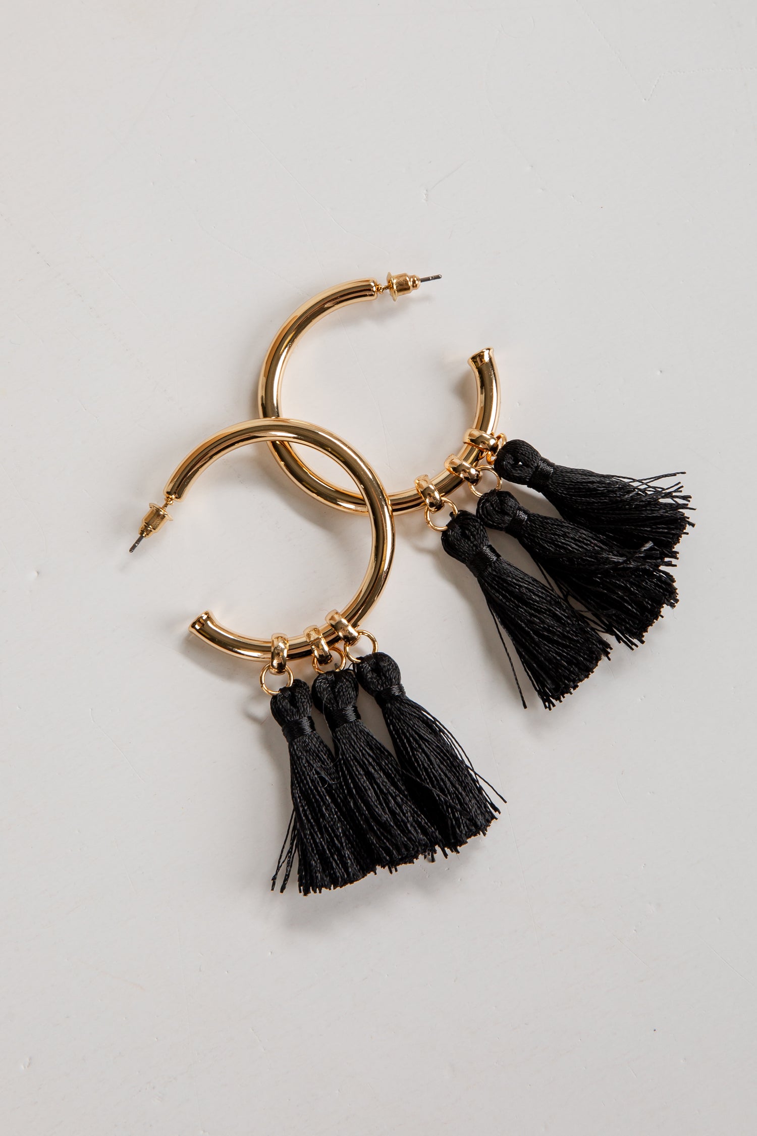 Gold hoop earrings with black tassels on a light gray background