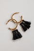 Gold hoop earrings with black tassels on a light gray background