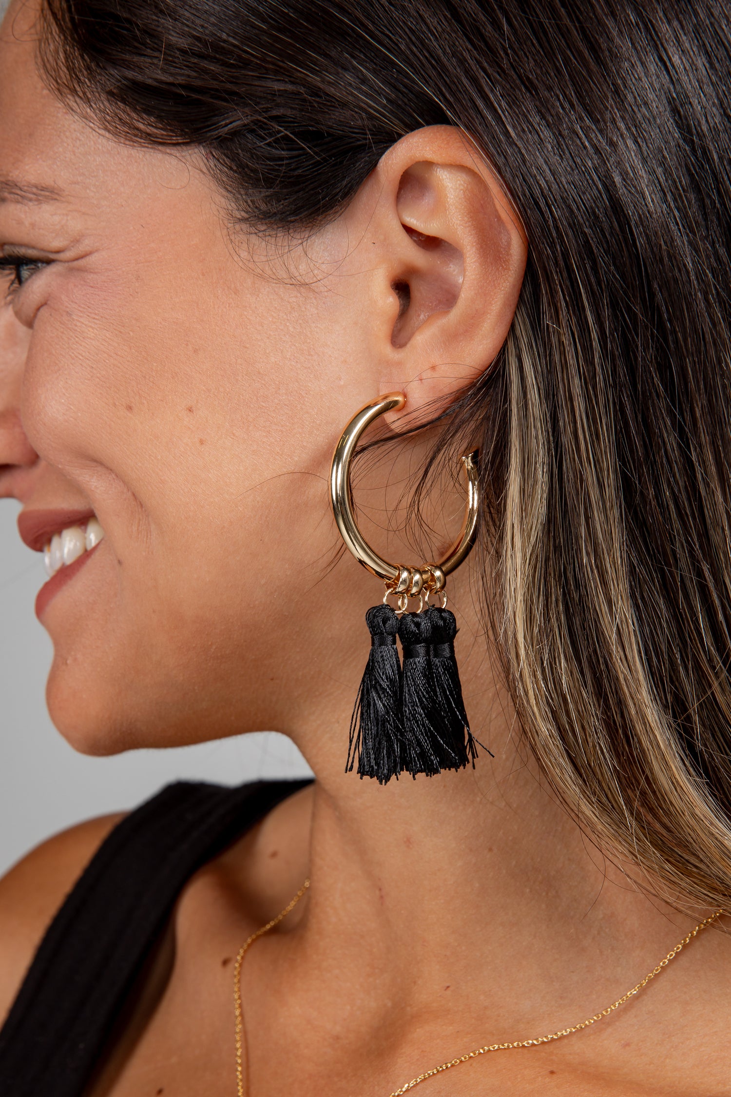 Woman wearing a gold hoop earring with black tassels against a neutral background