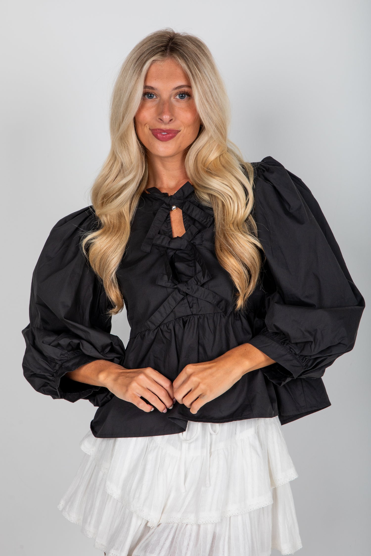 Woman wearing a black blouse with ruffled details and a white skirt on a plain background