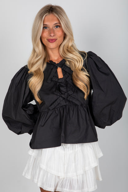 Woman wearing a black blouse with puffed sleeves and a white skirt on a gray background