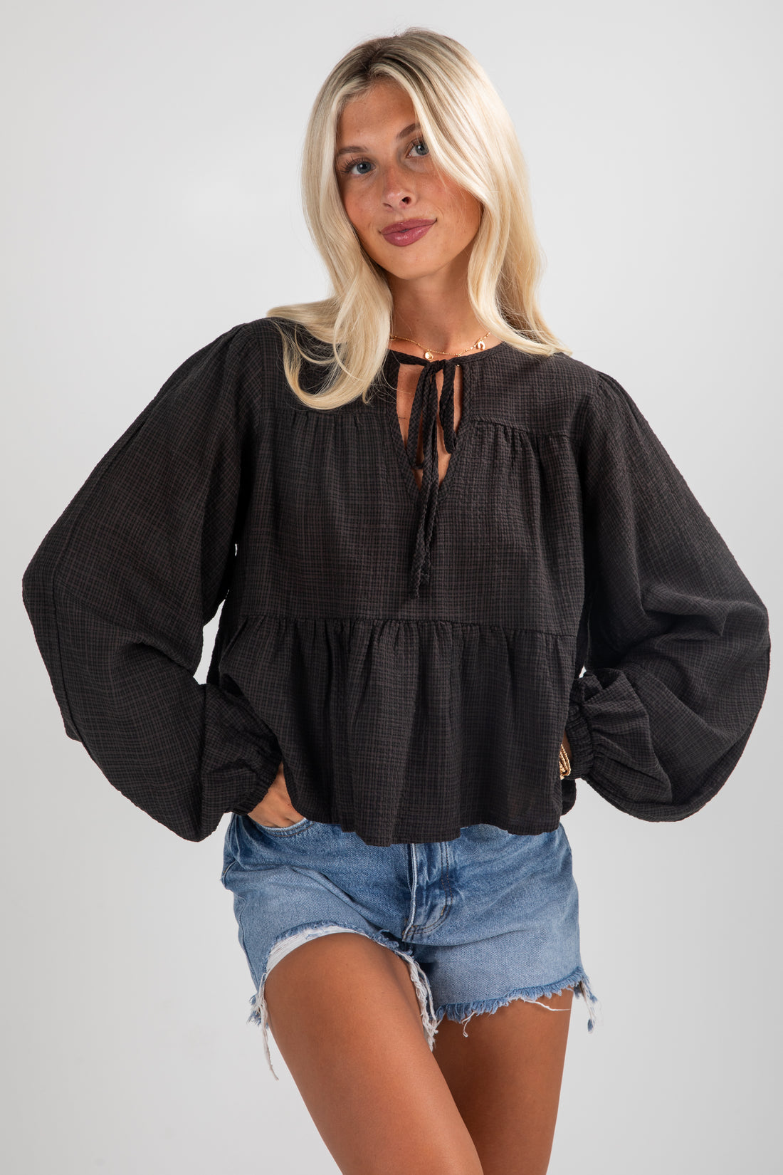 Woman wearing a black blouse with balloon sleeves and denim shorts on a plain background