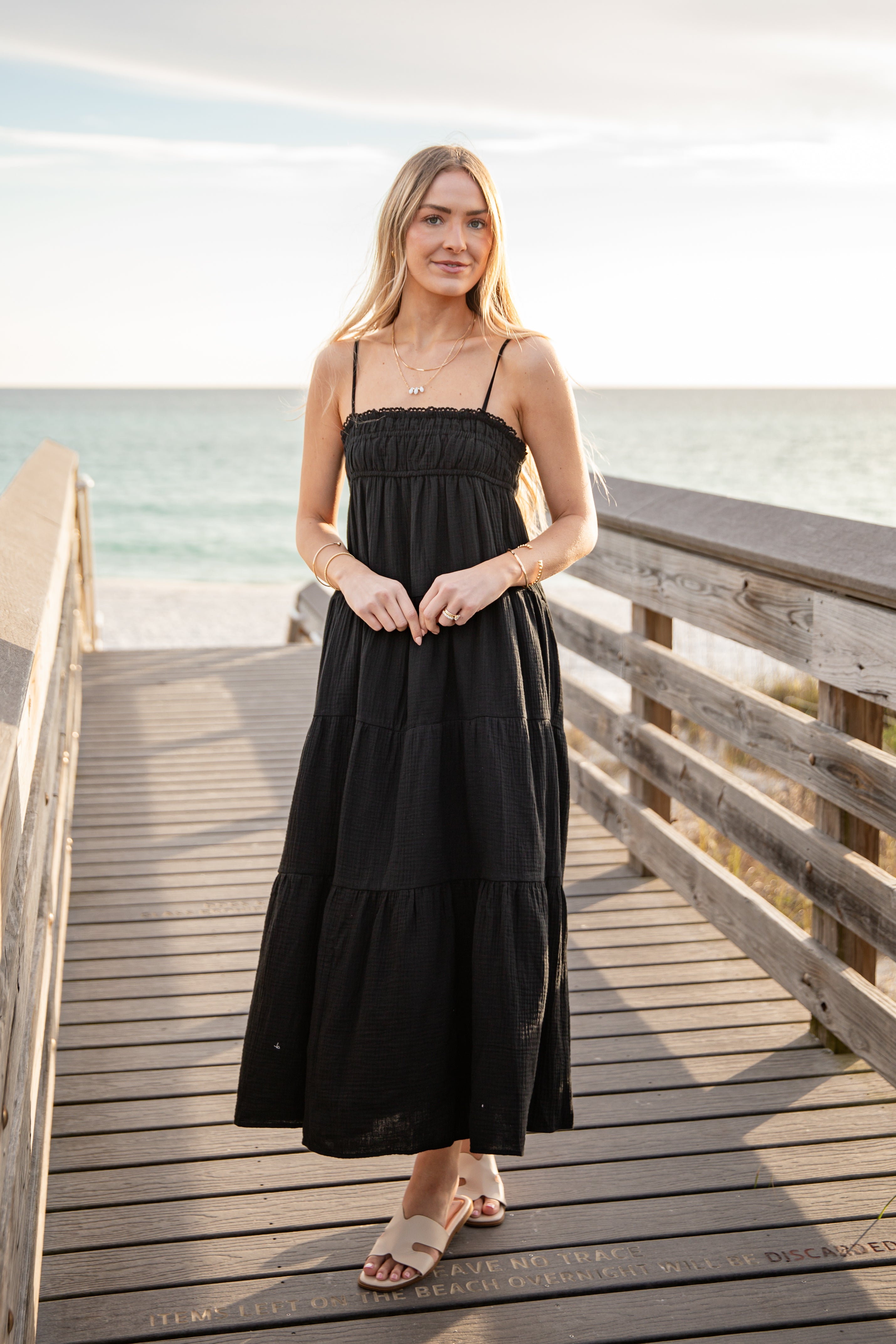 Woman in a black dress standing on a wooden pier by the ocean.