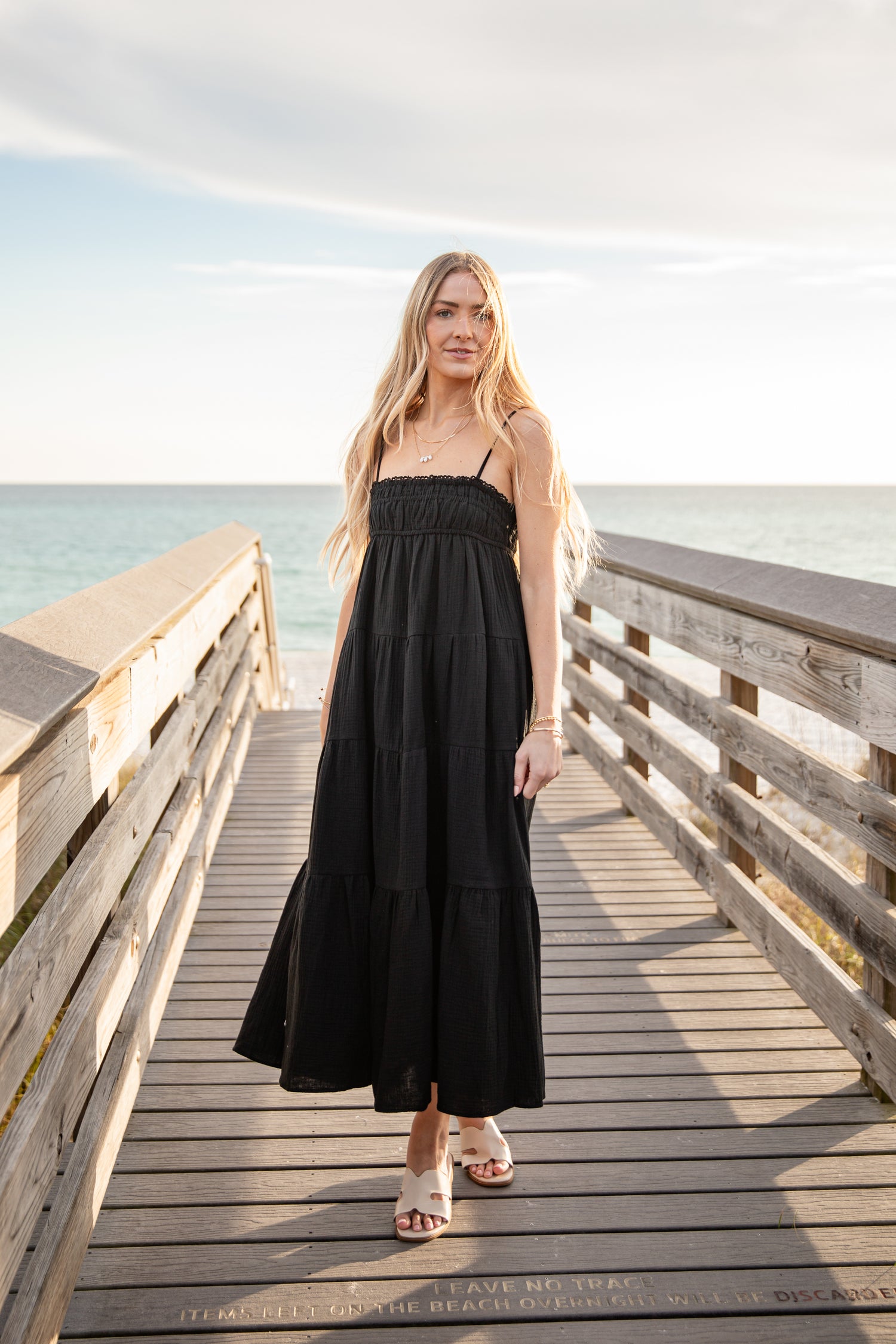 Woman in a black dress standing on a wooden pier by the ocean.