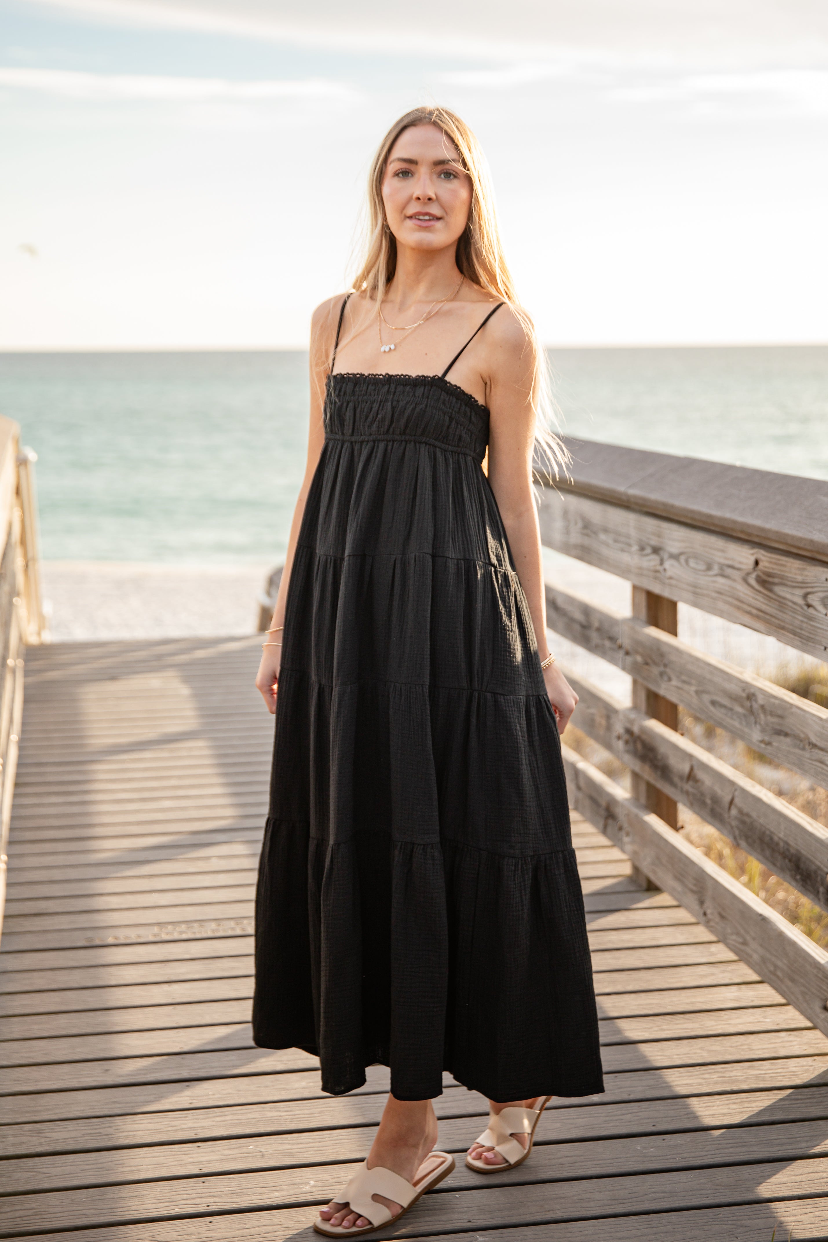 Woman in a black dress standing on a wooden pier by the water.