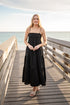 Woman in a black dress standing on a wooden pier by the ocean.