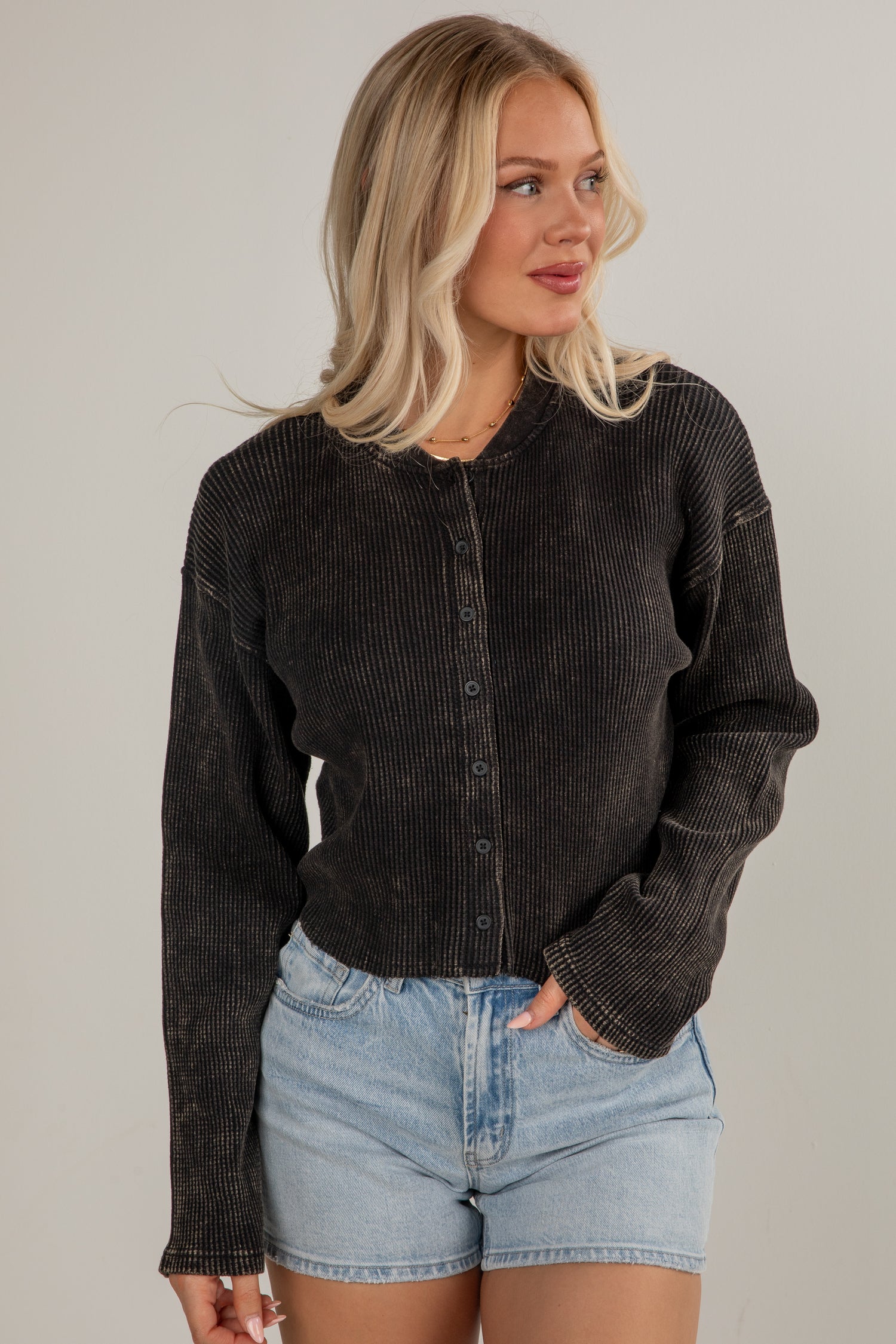 Woman wearing a black corduroy jacket and denim shorts on a plain background