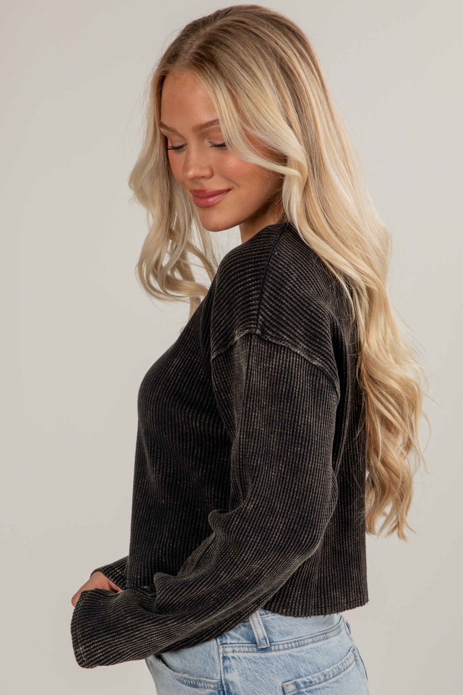 Woman wearing a dark ribbed sweater and light blue jeans against a plain background
