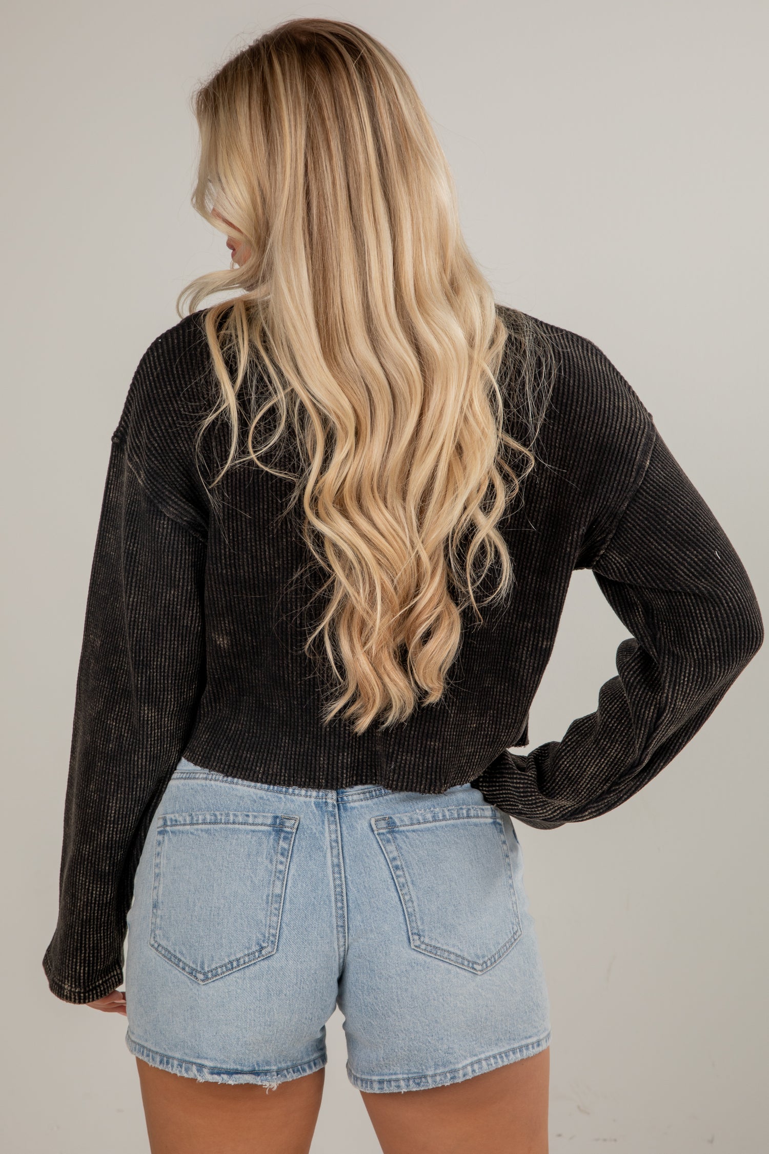 Person wearing a black corduroy jacket and light blue denim shorts on a plain background