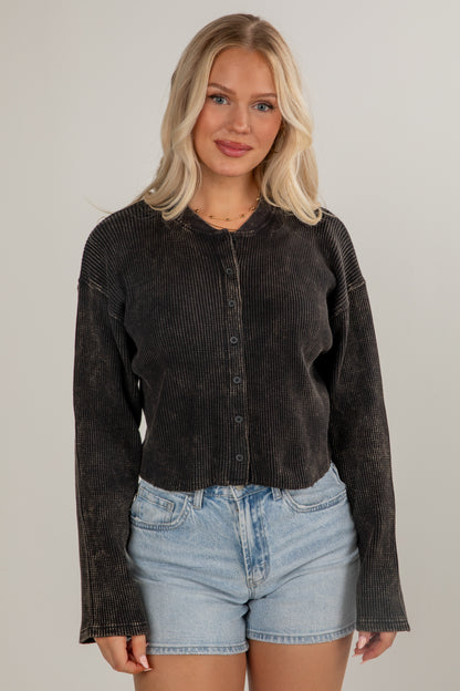 Woman wearing a dark corduroy shirt and denim shorts against a plain background