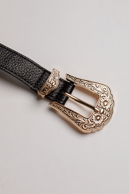 A close-up of a black textured leather belt with an ornate, engraved rose gold metal buckle, set against a plain light gray background.