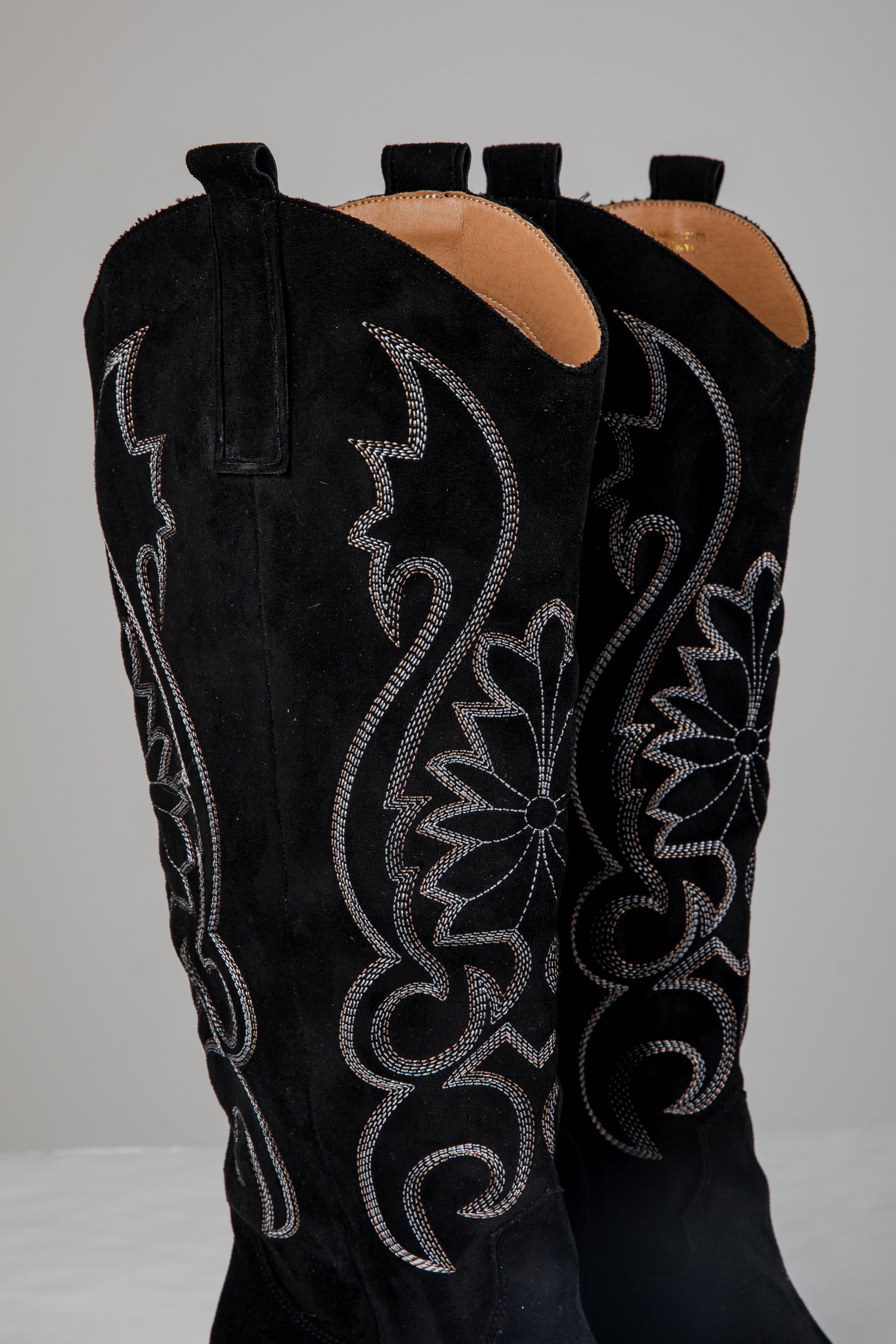 Black cowboy boots with intricate silver embroidery on a white background