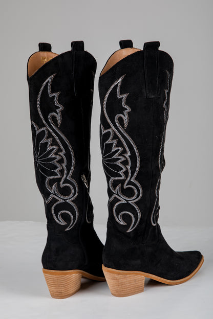 Black cowboy boots with intricate white embroidery on a gray background