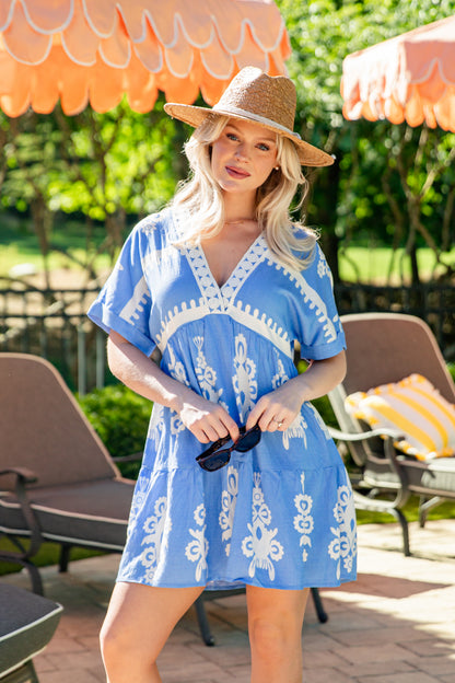 Woman in a blue dress with white patterns and a straw hat standing outdoors under orange umbrellas.
